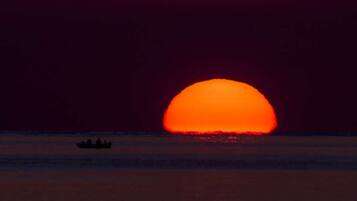 Um pôr do sol sobre águas calmas com um pequeno barco ao primeiro plano.