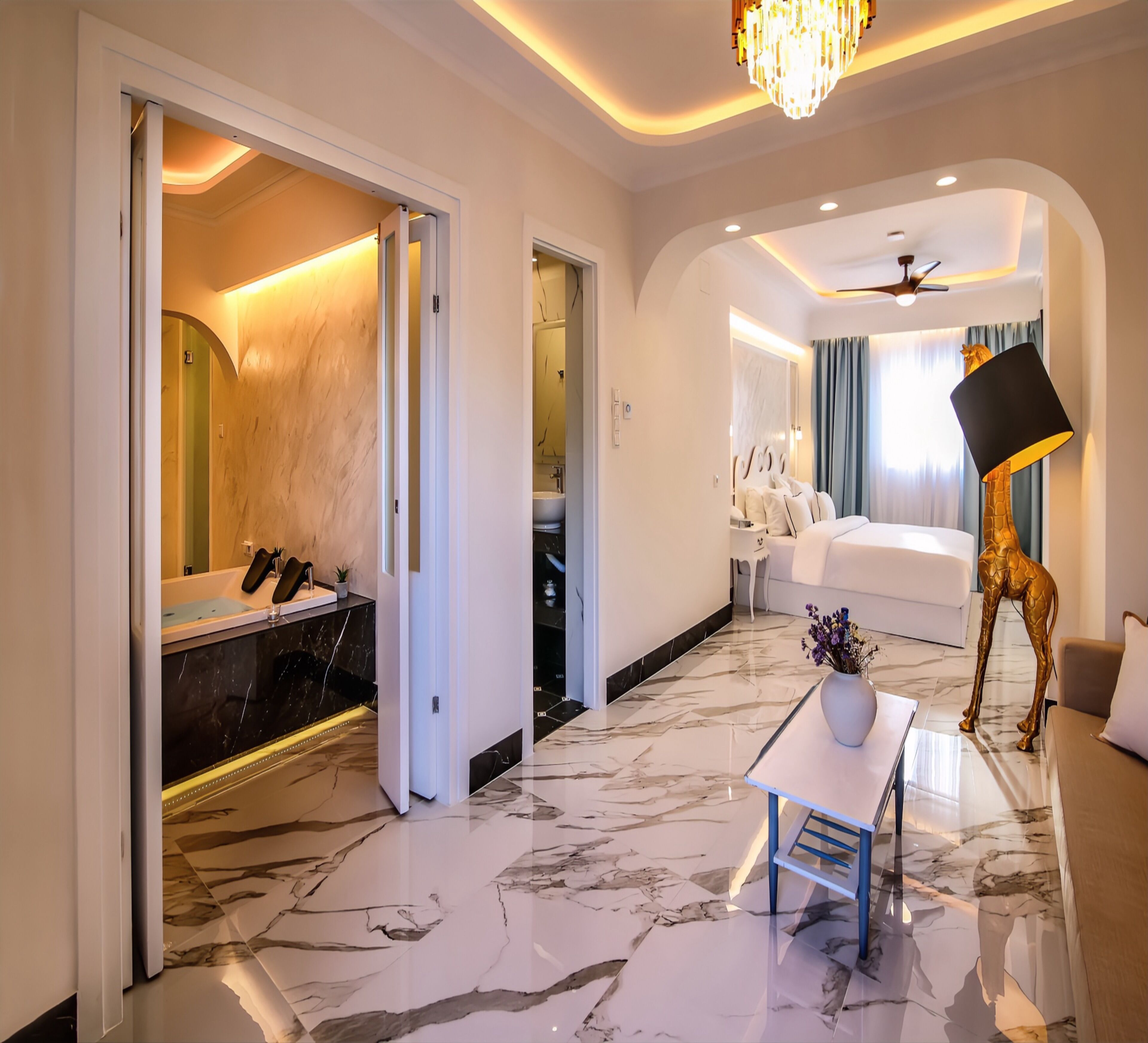 A modern hotel room with a marble floor, a bed, a desk with a lamp, and a giraffe statue.