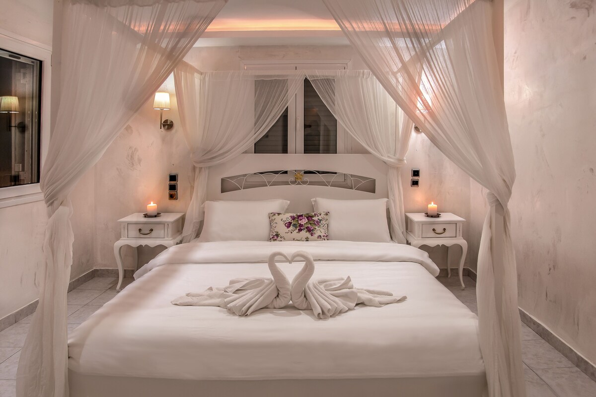 A bedroom with a canopy bed, bedside lamps, and a decorative swan towel arrangement.