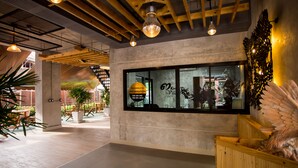 A modern interior with exposed wooden beams, a concrete wall with a glass window displaying a logo and contact information, and potted plants. - 3 Kwan Village (Chonburi)