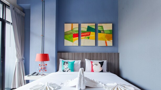 Una habitación de hotel con cama, mesita de noche, lámpara y ventana con cortinas.