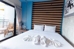 A hotel room with a wooden headboard, a bed with white linens, two towels on the bed, a nightstand with a lamp and phone, and a view of the outside balcony. - 3 Kwan Village (Chonburi)