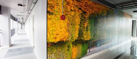 Un pasillo con un gran mural que representa follaje otoñal, piso pulido y techo con conductos y luminarias a la vista.