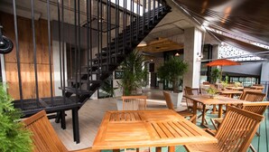 A modern interior with wooden tables and chairs, a staircase, and potted plants. - 3 Kwan Village (Chonburi)