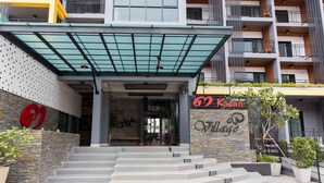 A modern building with a stone facade, a large entrance with steps, and a sign for 'Kwan Village'. - 3 Kwan Village (Chonburi)