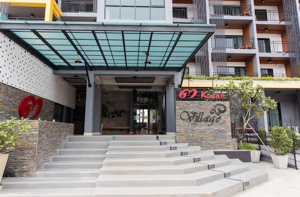 A modern building with a stone facade, a large entrance with steps, and a sign for 'Kwan Village'. - 3 Kwan Village (Chonburi)