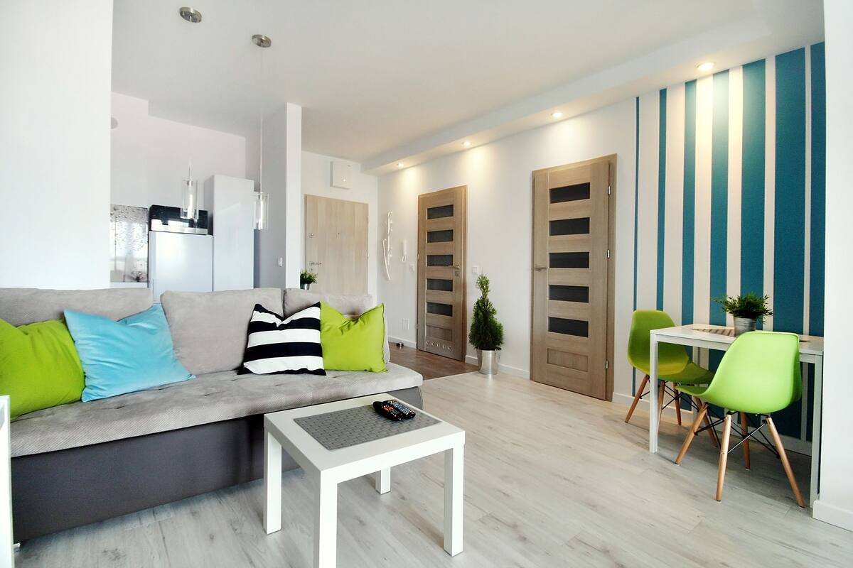 A modern living room with a grey sofa, a white coffee table, and a dining area with a white table and green chairs.