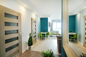 A modern hotel room with a wooden wardrobe, a small desk with a chair, a bed, and a large mirror. - LIVIN Apartments (Szczecin)