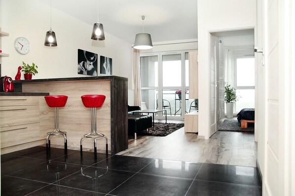 A modern kitchen with black tiles, two red bar stools, pendant lights, and a wooden countertop.