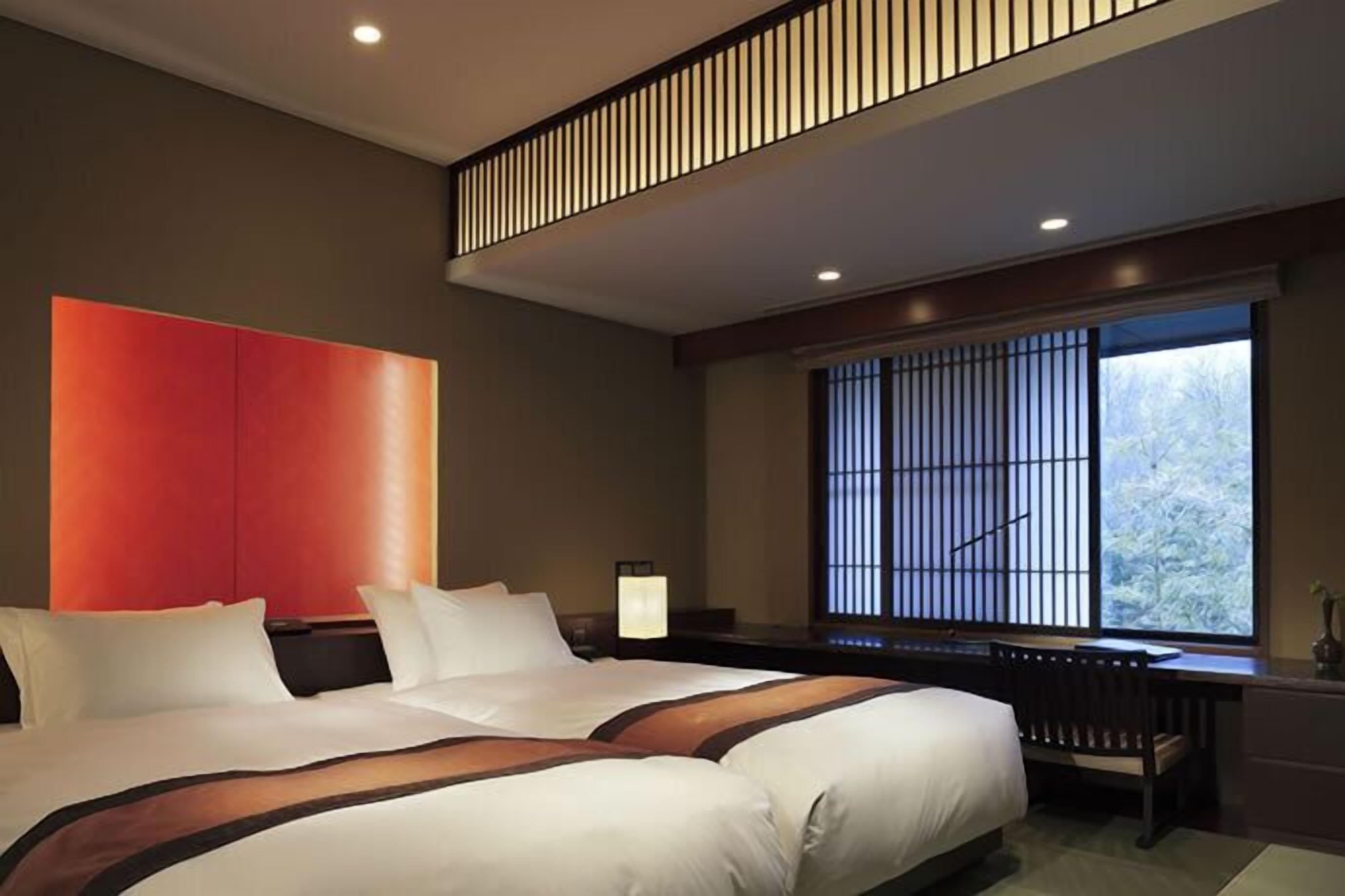 A modern hotel room with a large bed, a desk, and a window with a view of trees.
