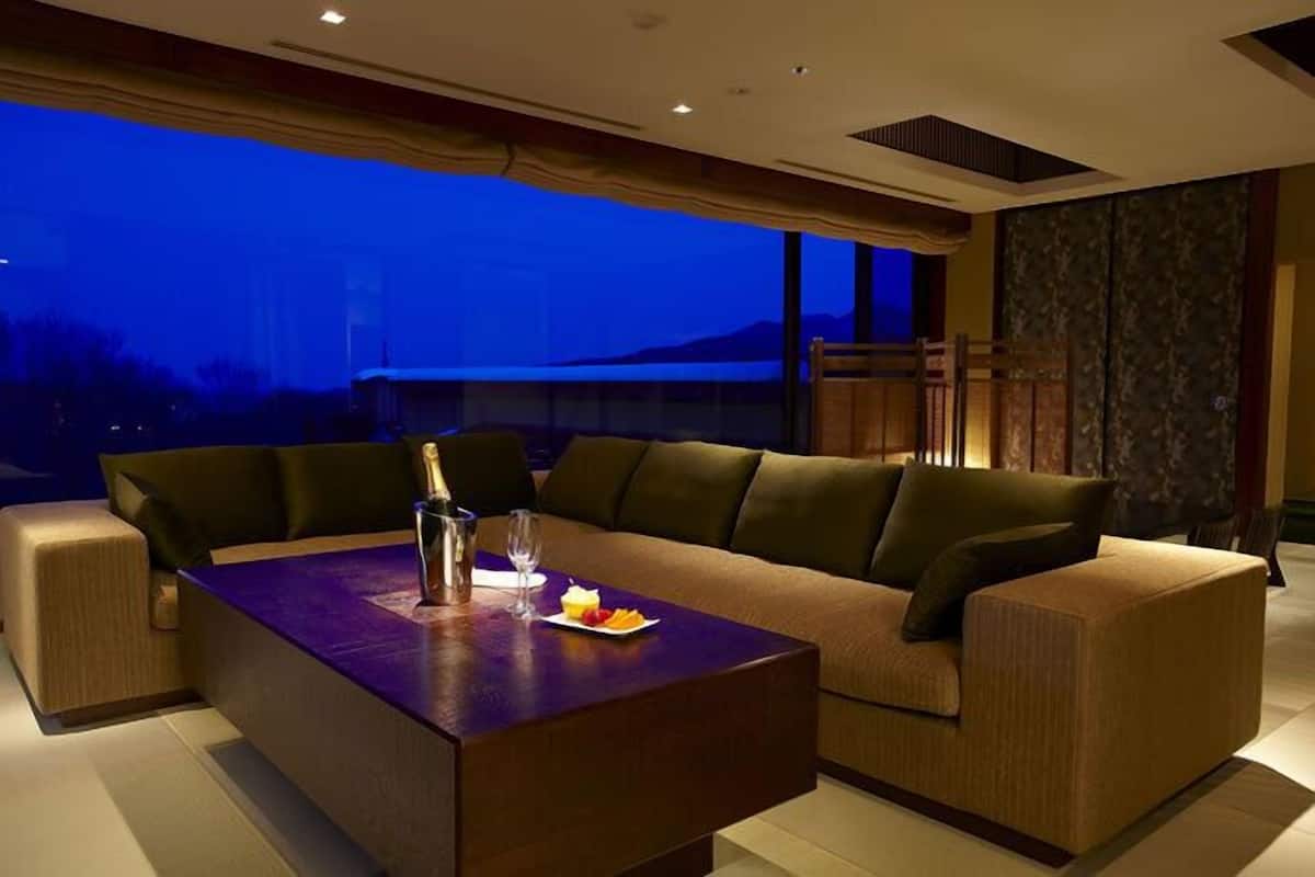 A modern living room with a sofa and a coffee table, a bottle of champagne, and a plate of fruit.