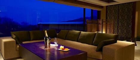A modern living room with a sofa and a coffee table, a bottle of champagne, and a plate of fruit.