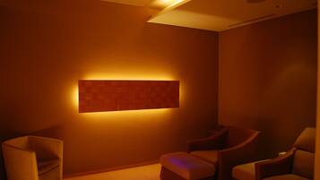 A dimly lit room with a modern design, featuring a wall-mounted light panel and two cushioned chairs.