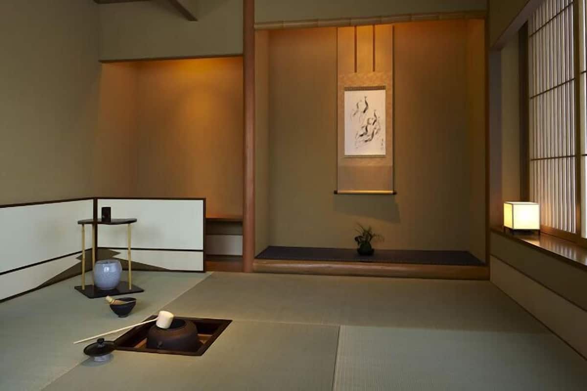 A traditional Japanese room with tatami flooring, a low table with a tea set, a shoji screen, and a hanging scroll.
