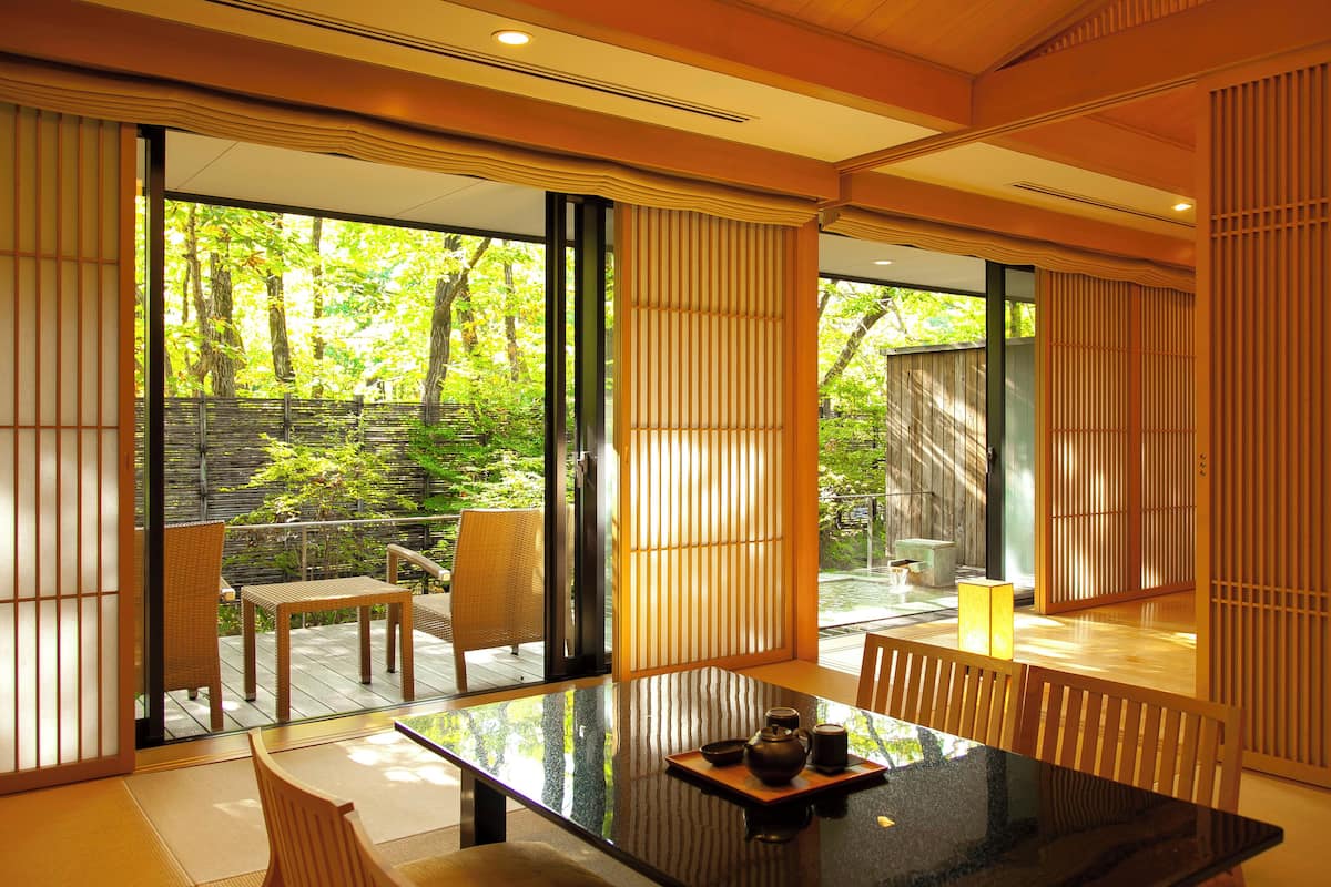 A modern interior with a glass table, wooden chairs, and a view of a garden.