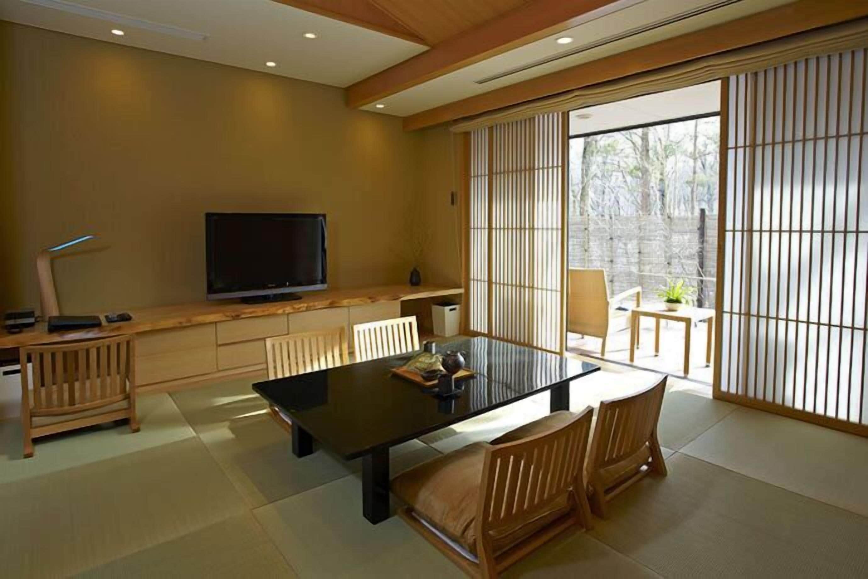 A traditional Japanese-style room with tatami flooring, a low table with cushions, a television, and sliding doors leading to an outdoor area.