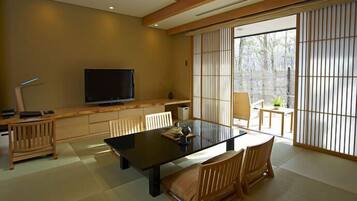 A traditional Japanese-style room with tatami flooring, a low table with cushions, a television, and sliding doors leading to an outdoor area.
