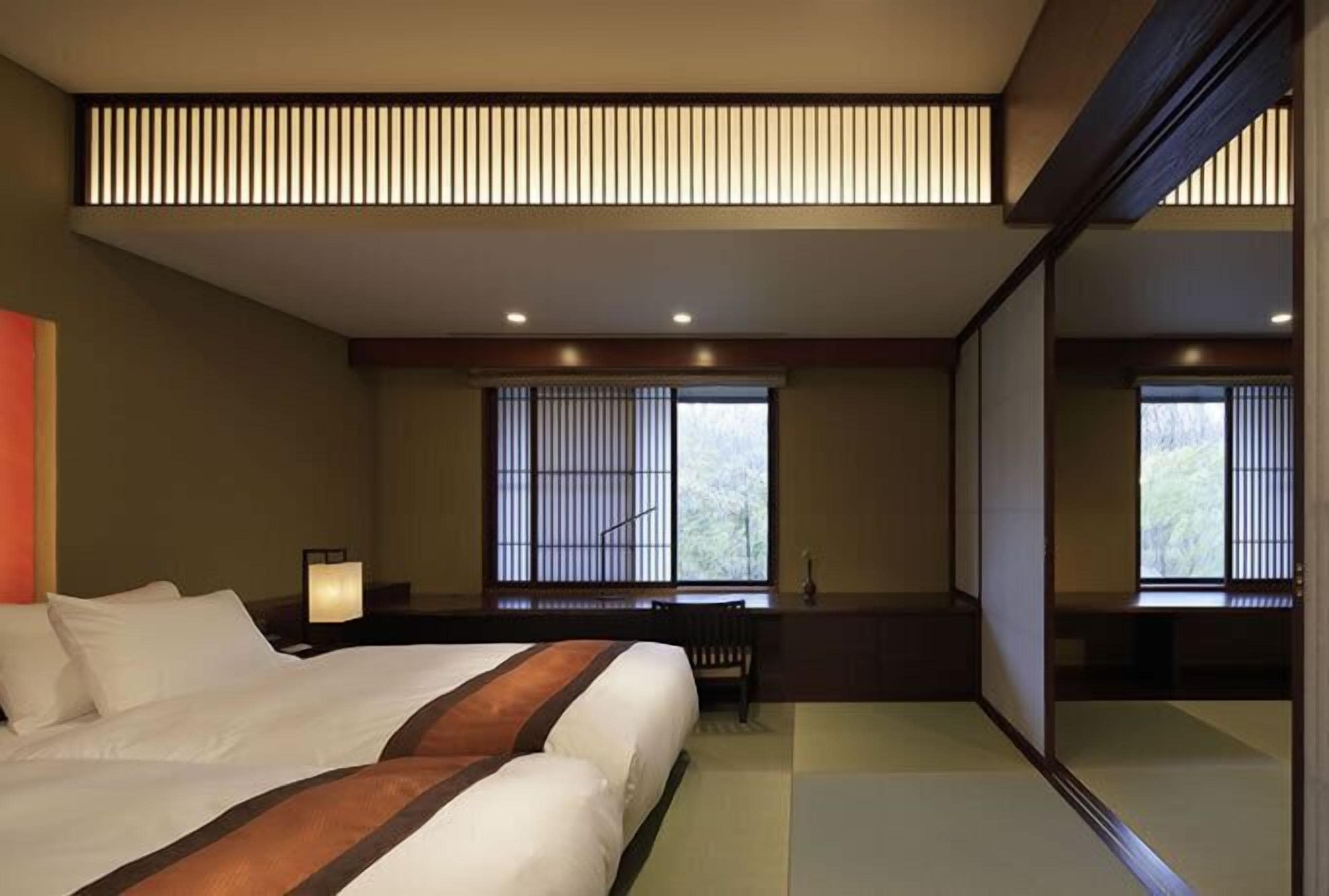A hotel room with a large bed, a desk, and a window with blinds.