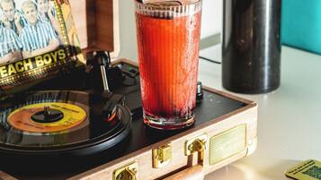 Un tocadiscos de madera con un disco de vinilo, un vaso con una bebida roja y una lámpara al fondo.
