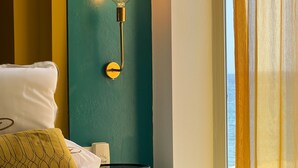 A hotel room with a bed, pillows, a bedside table, a lamp, and a window with curtains.