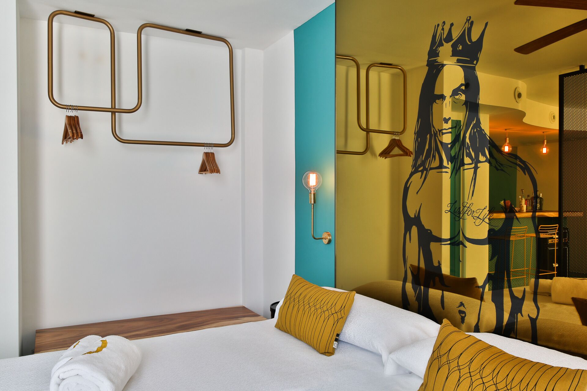 A hotel room with a bed, a wall-mounted light fixture, and a large decorative mirror.