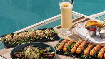 A dining table by a pool with a meal consisting of dumplings, grilled chicken skewers, and a salad.