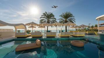 A pool area with lounge chairs, umbrellas, and palm trees.
