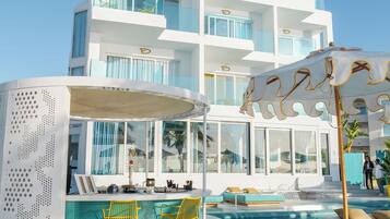 Un hotel moderno con zona de piscina, mobiliario exterior y un edificio grande con balcones.