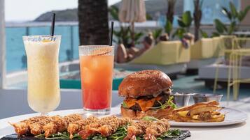 Une table dressée avec un repas, deux boissons et une vue sur la mer et les palmiers.