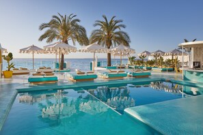 A pool area with lounge chairs and umbrellas, palm trees, and a view of the sea. - Dorado Ibiza - Adults Only (Sant Josep de sa Talaia)