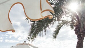 A sunlit outdoor seating area with lounge chairs, umbrellas, and a view of the sea.