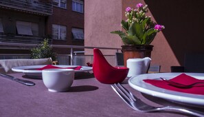 A table set with white plates, red napkins, and a red bowl, with a potted plant and a white pitcher on the balcony. - Domus Raffaello suite in Rome (Rome)