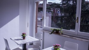 A room with a white table and chairs, a window with a view of buildings and trees, and a sign reading "DR DOMUS RAIATELLO". - Domus Raffaello suite in Rome (Rome)