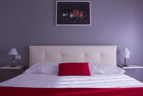 A neatly made bed with white and red bedding, two bedside tables with lamps, and a framed artwork on the wall. - Domus Raffaello suite in Rome (Rome)