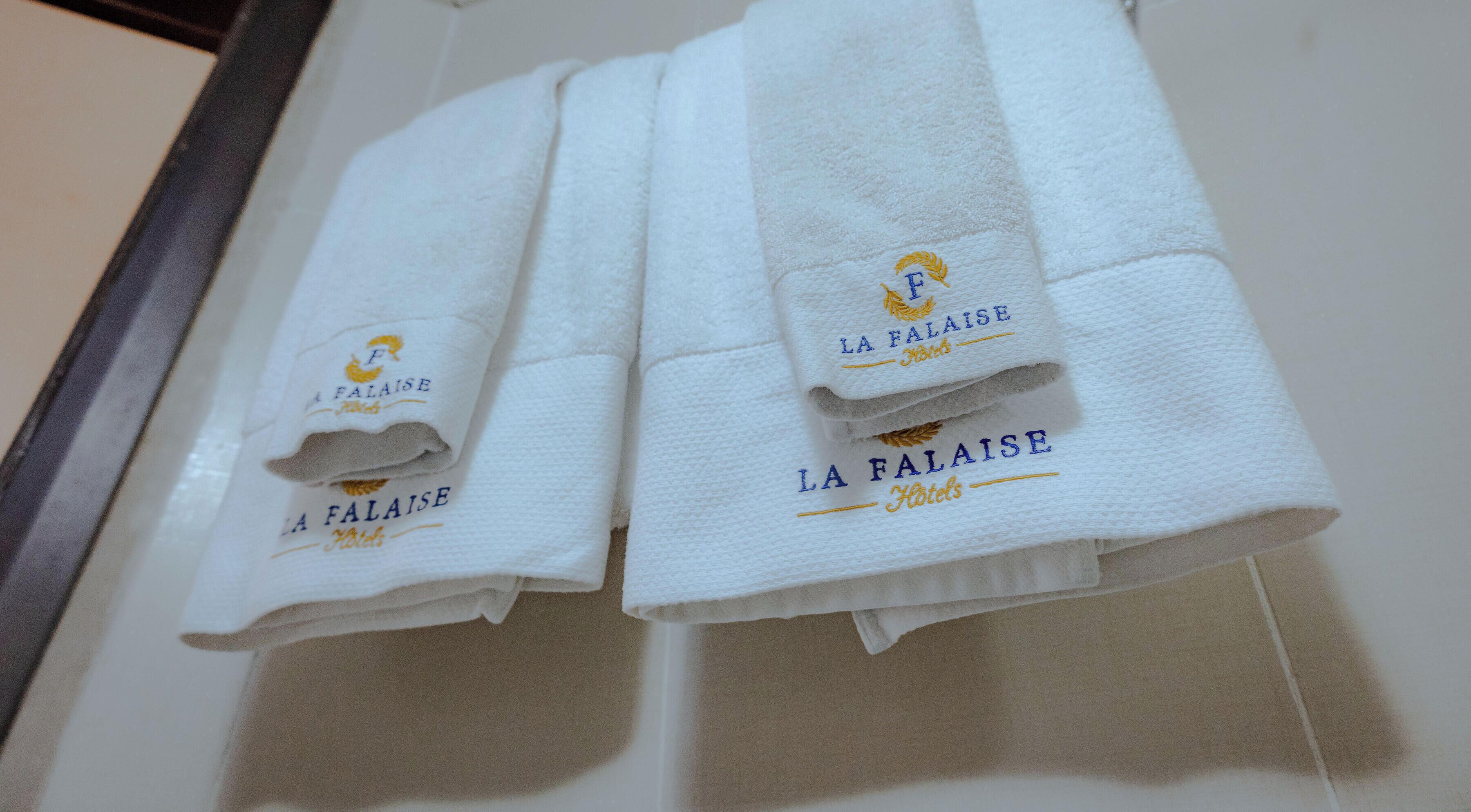 Two folded white towels with embroidered text and a logo, placed on a tiled surface.
