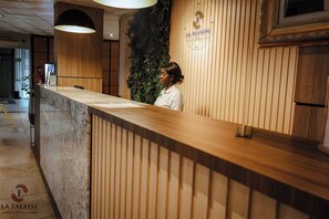Un mostrador de recepción con detalles de madera, un logotipo en la pared y un cartel que indica la ubicación del salón de banquetes.