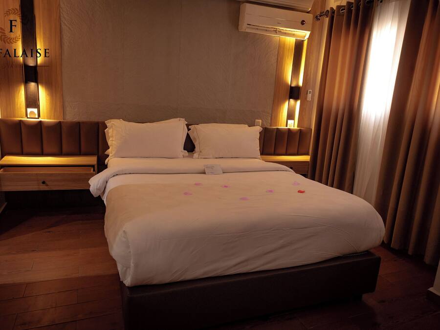 Une chambre d’hôtel avec un grand lit, deux tables de chevet, un climatiseur fixé au mur et une fenêtre avec des rideaux.
