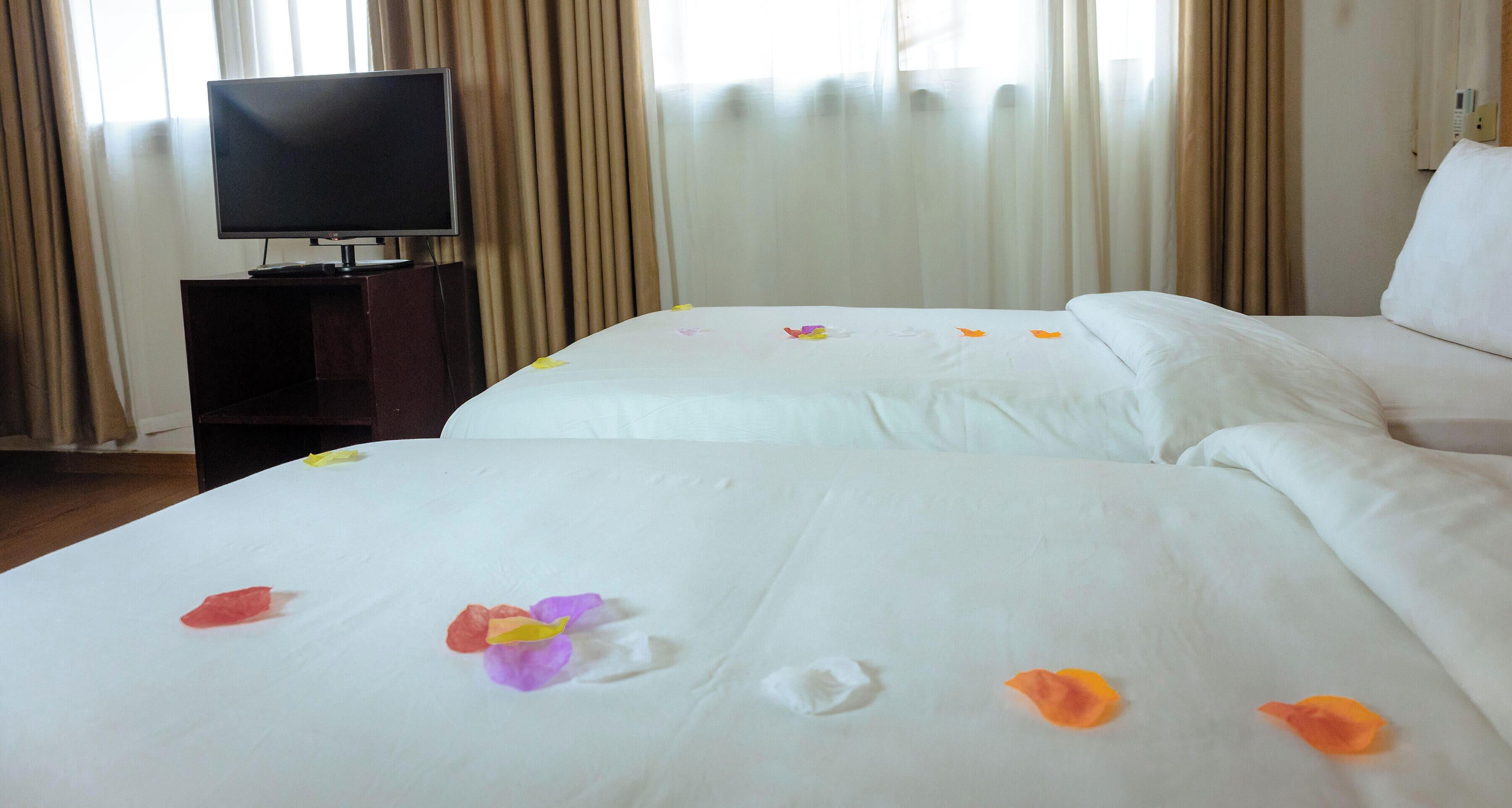 Quarto de hotel com duas camas, uma televisão em um suporte e cortinas.