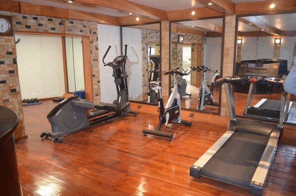 Un gimnasio con varios equipos de ejercicio, incluyendo cintas de correr, bicicletas estáticas y una máquina elíptica.