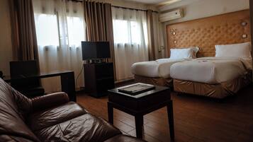 A hotel room with a leather sofa, a TV on a stand, two beds with white bedding, and a wooden headboard.