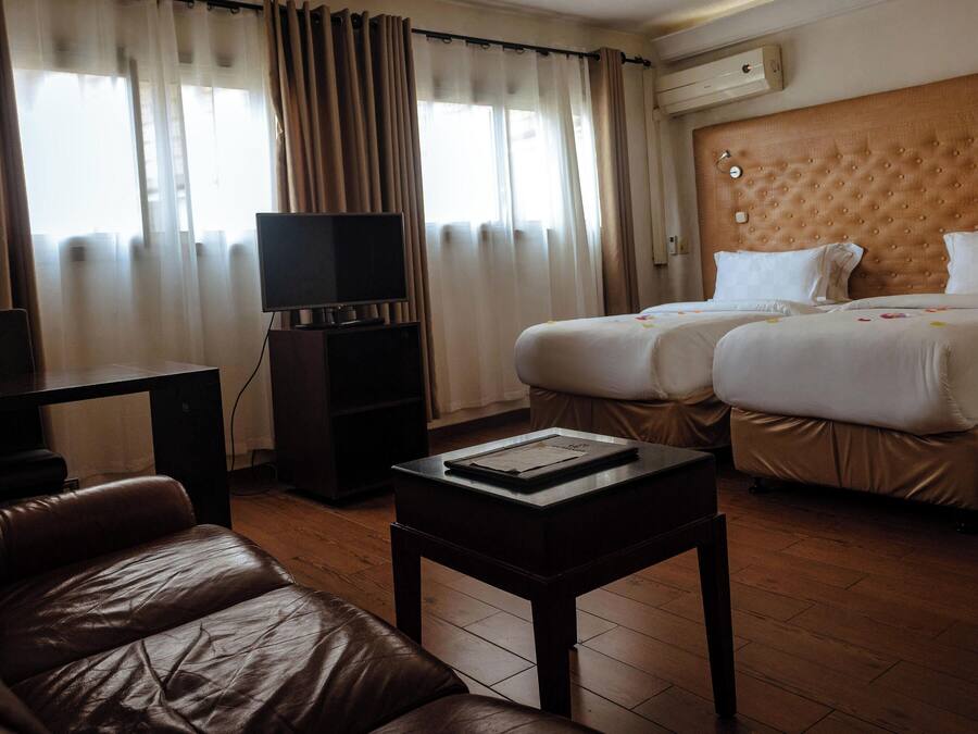 A hotel room with a leather sofa, a TV on a stand, two beds with white bedding, and a wooden headboard.