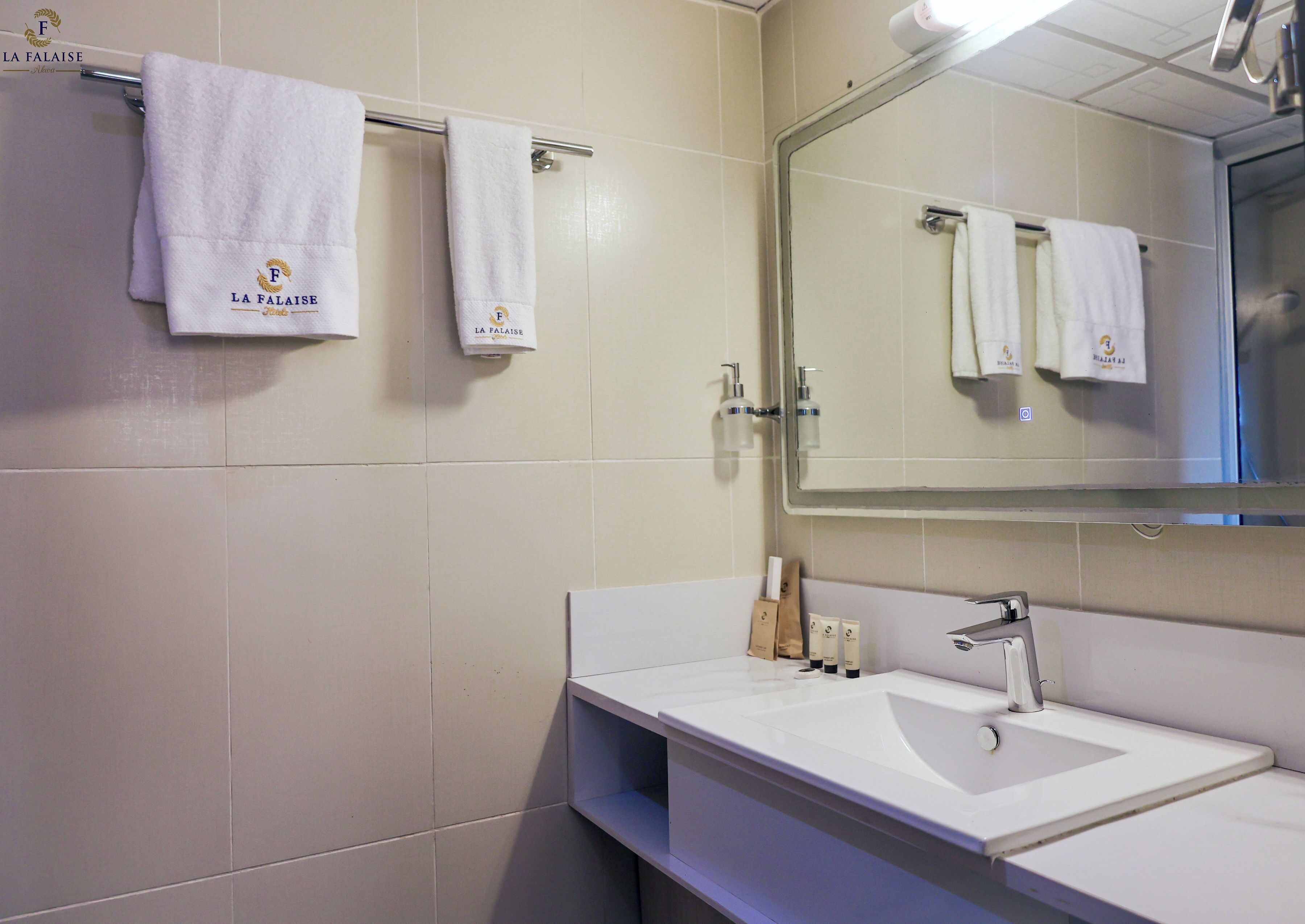 Une salle de bain avec un lavabo blanc, un miroir et deux serviettes suspendues à un porte-serviettes.