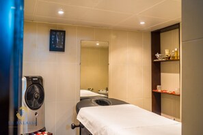 Habitación de hotel con cama, ventilador, espejo y repisas con artículos de aseo.