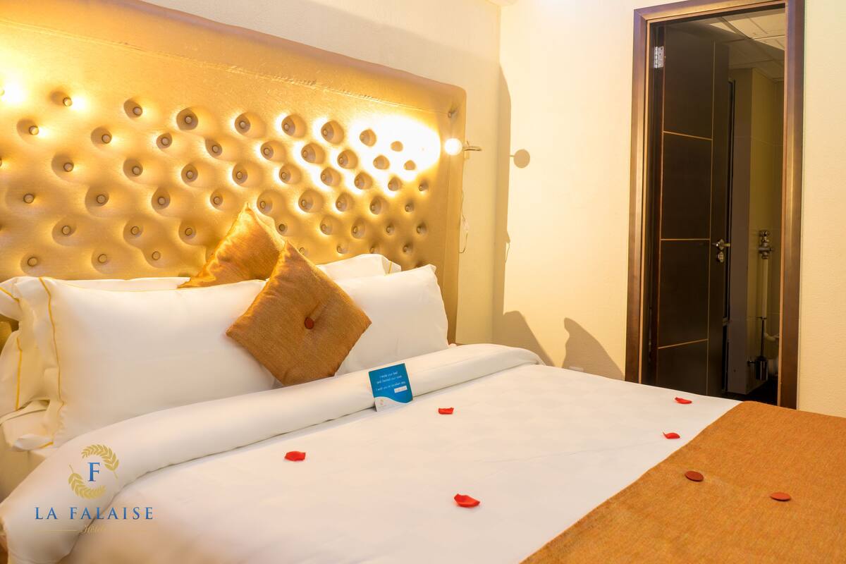 A hotel room with a tufted headboard, white bedding, a brown throw blanket, and a visible door.