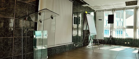 A spacious room with a large white projection screen, a glass podium, and a projection screen on a tripod stand.