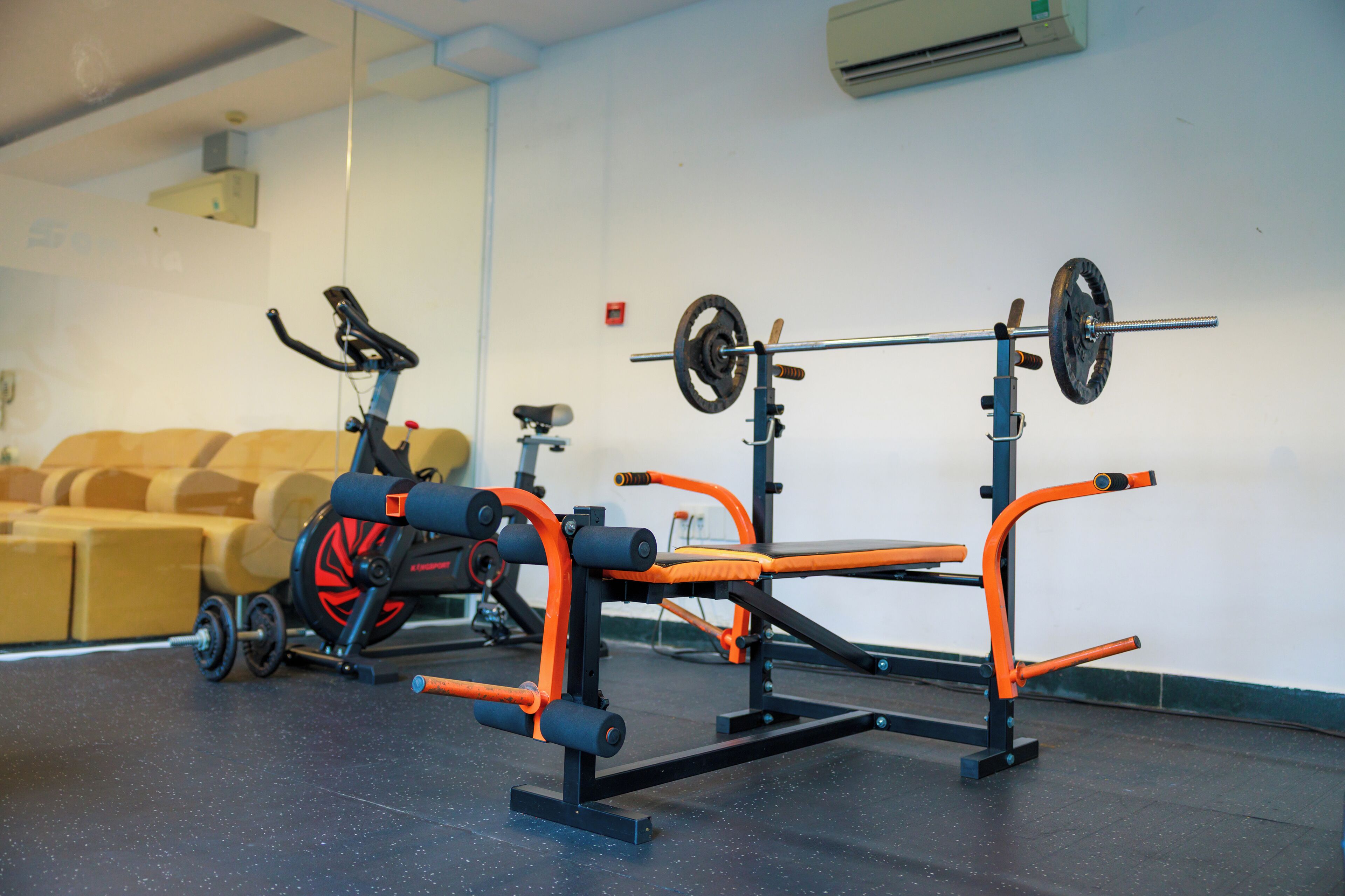 Uma academia com equipamentos de exercício, um banco e um ar condicionado fixado na parede.