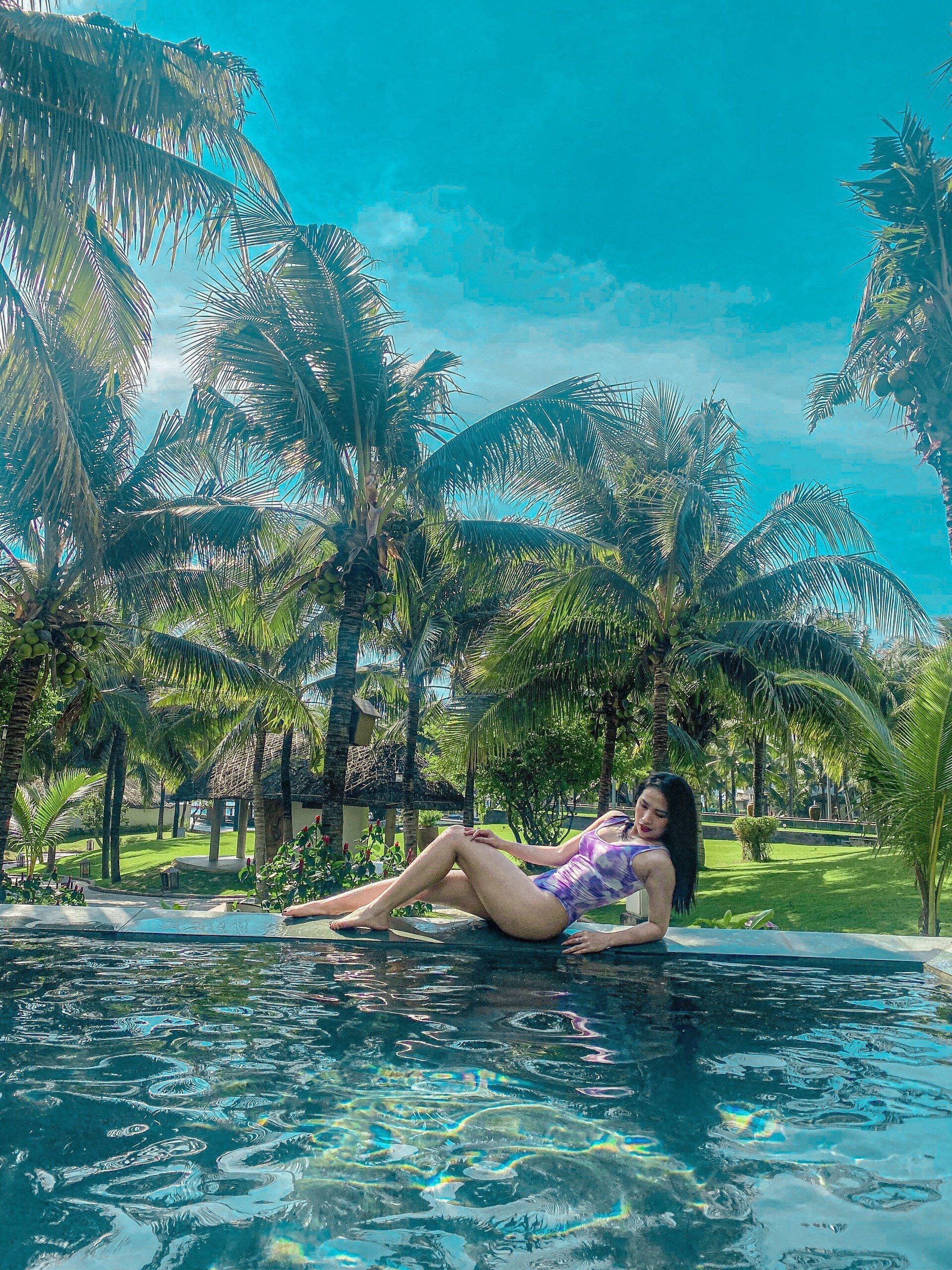 Una persona descansando junto a una piscina rodeada de palmeras.