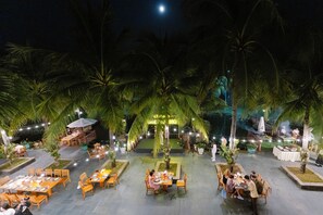 An outdoor dining area with tables and chairs, surrounded by palm trees and a sign indicating a local BBQ. - Sonata Resort & Spa (Tien Thanh)