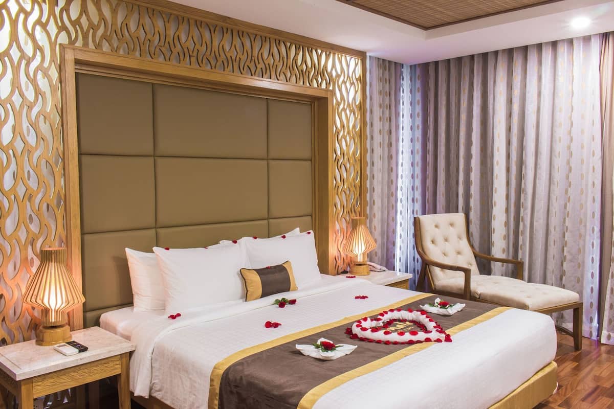 A hotel room with a large bed, a chair, a nightstand, and a decorative wall panel.
