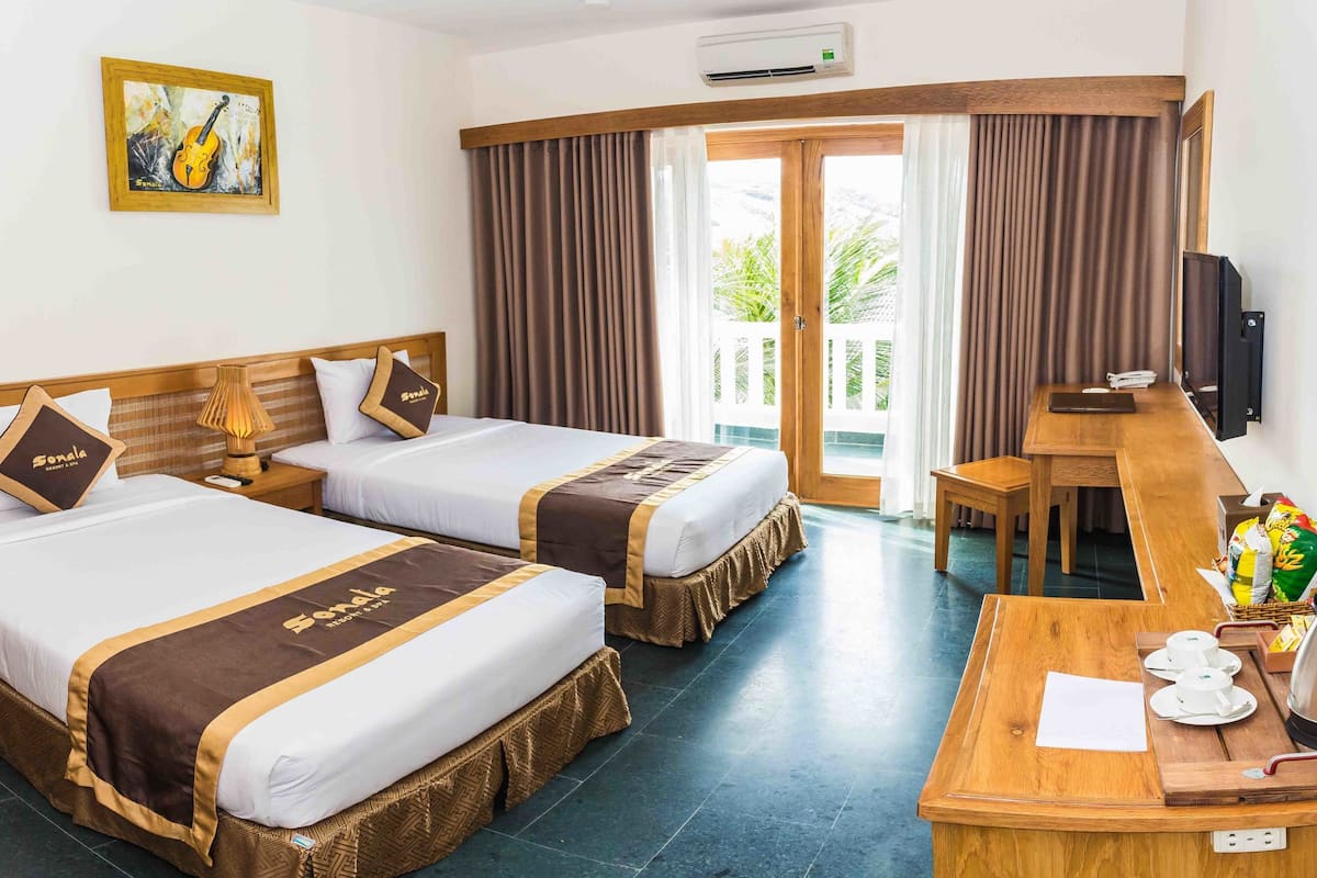 A hotel room with two beds, a desk, a television, and a window with curtains.